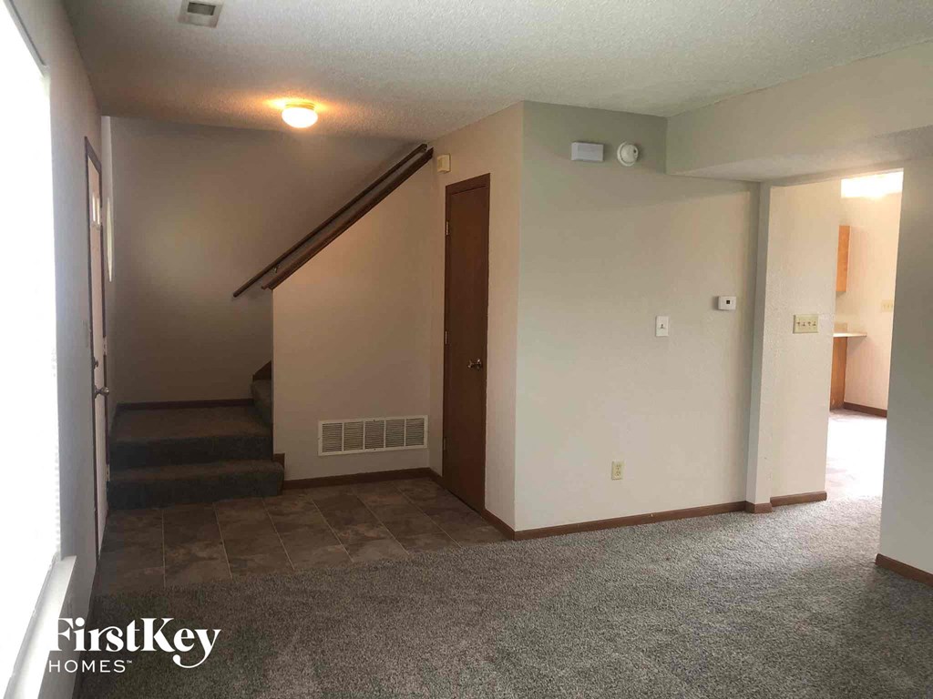 an empty living room with stairs and a door to a hallway