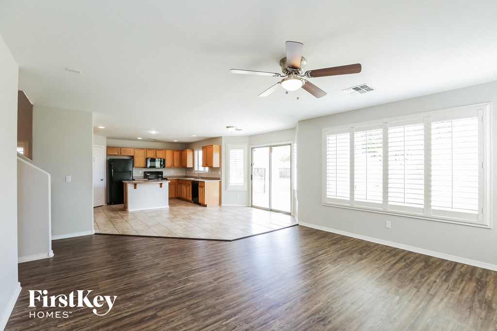 an empty living room with a ceiling fan and a kitchen