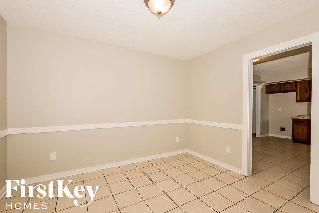 a empty living room with a tile floor and a door to the kitchen