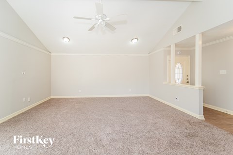 A spacious room with a carpeted floor and a ceiling fan.