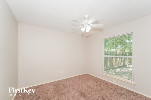 A room with a ceiling fan and a window showing trees outside.