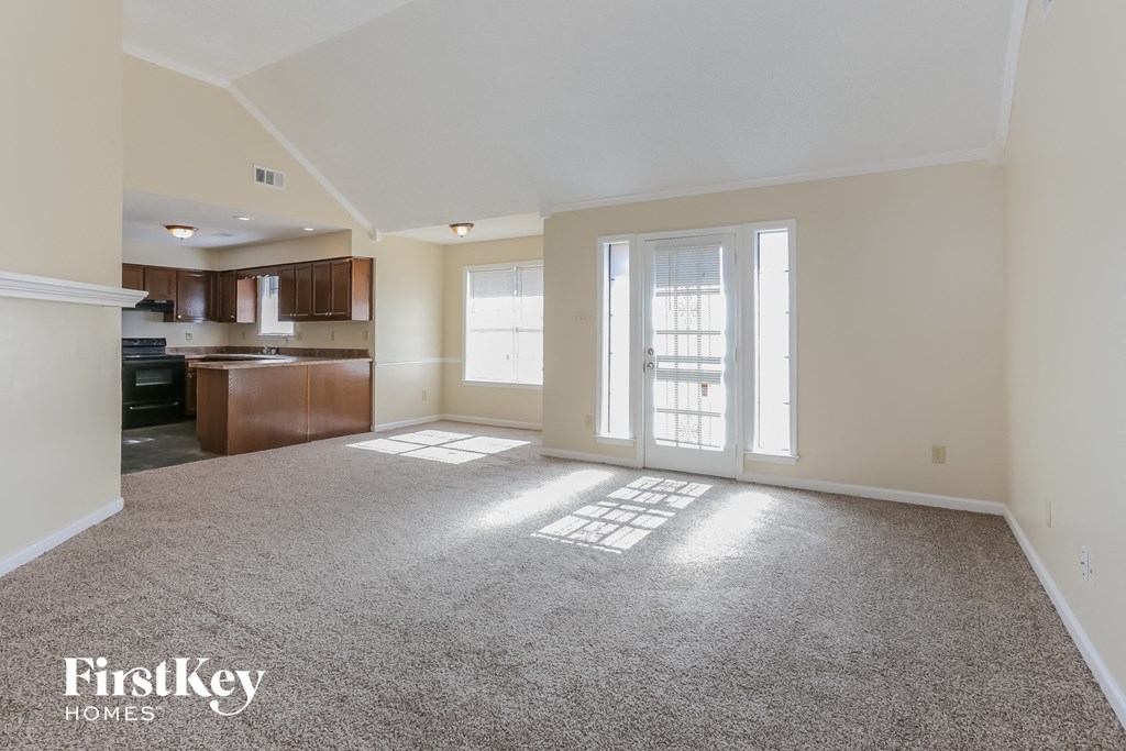 an empty living room with a kitchen in the background