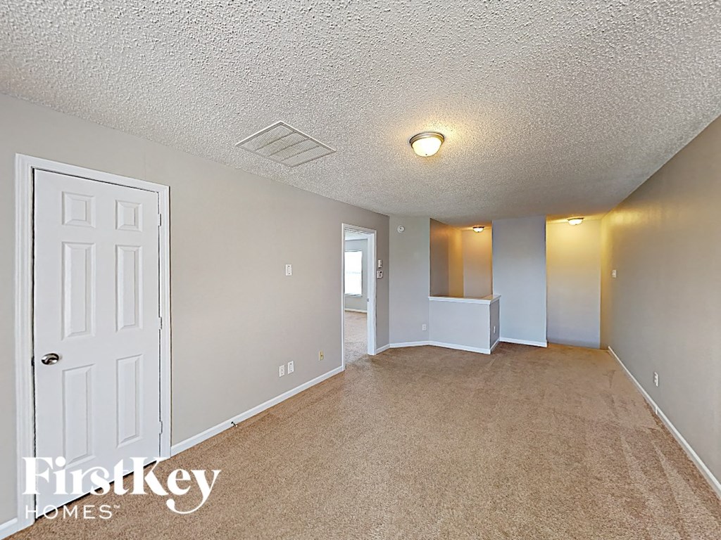 A white door is on the left side of a room with a carpeted floor and a light on the ceiling.