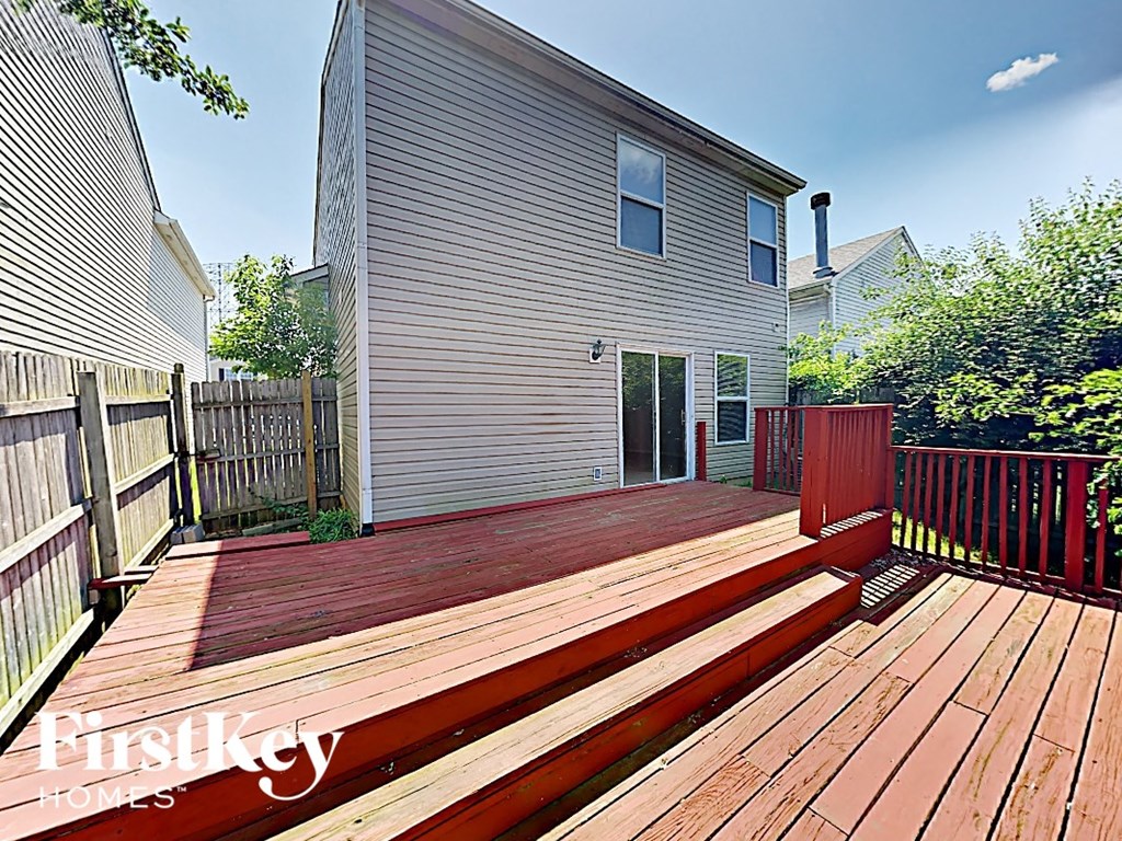 A wooden deck with a red railing and a house in the background.