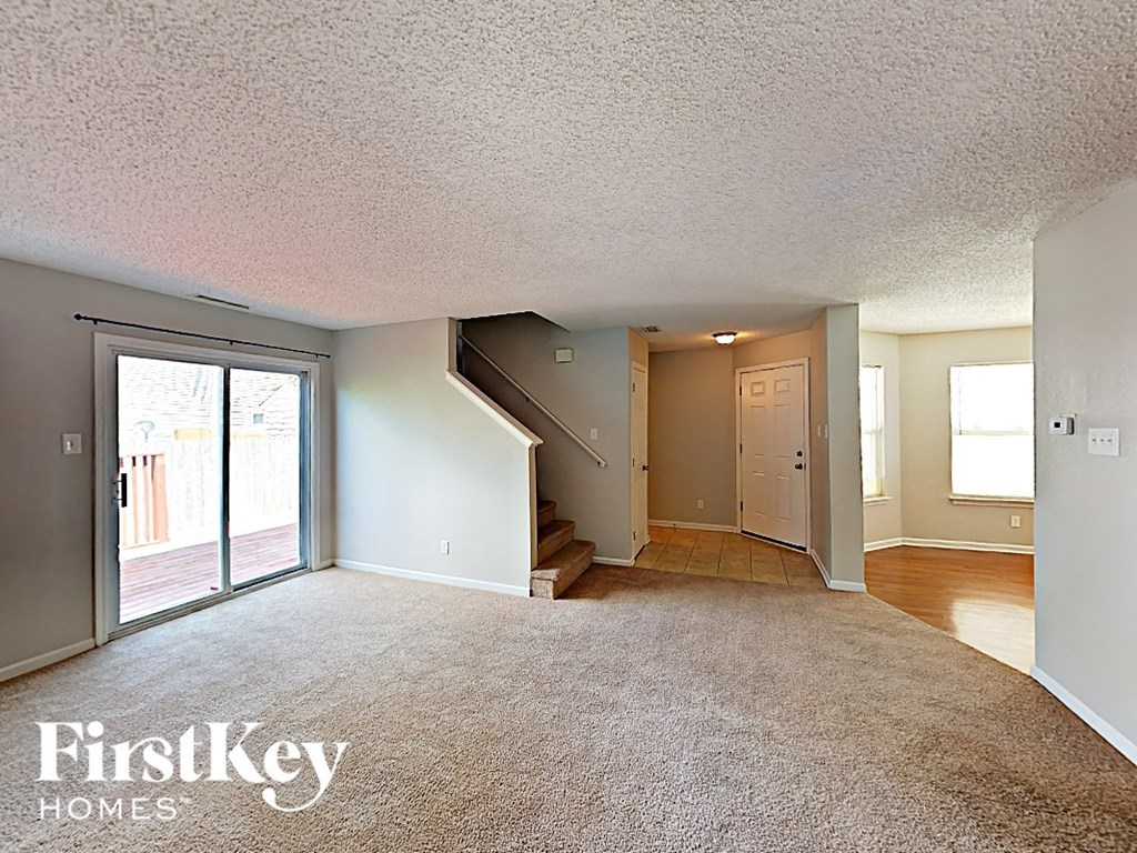A carpeted room with a staircase leading to the second floor.