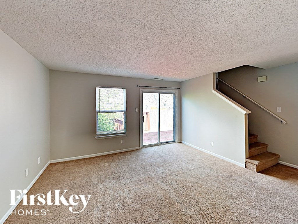 A carpeted room with a staircase leading to another room.