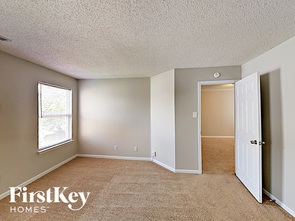 A room with a carpet floor and a doorway leading to another room.