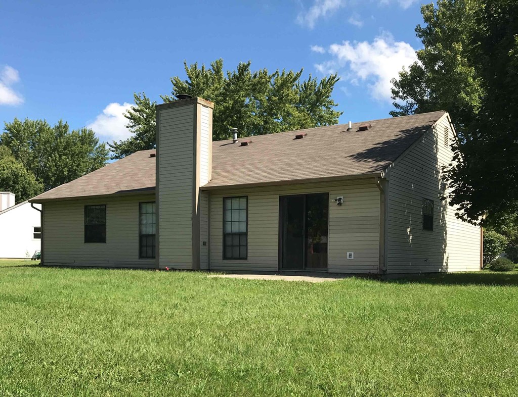 A house with a brown roof and a chimney is surrounded by a grassy lawn.