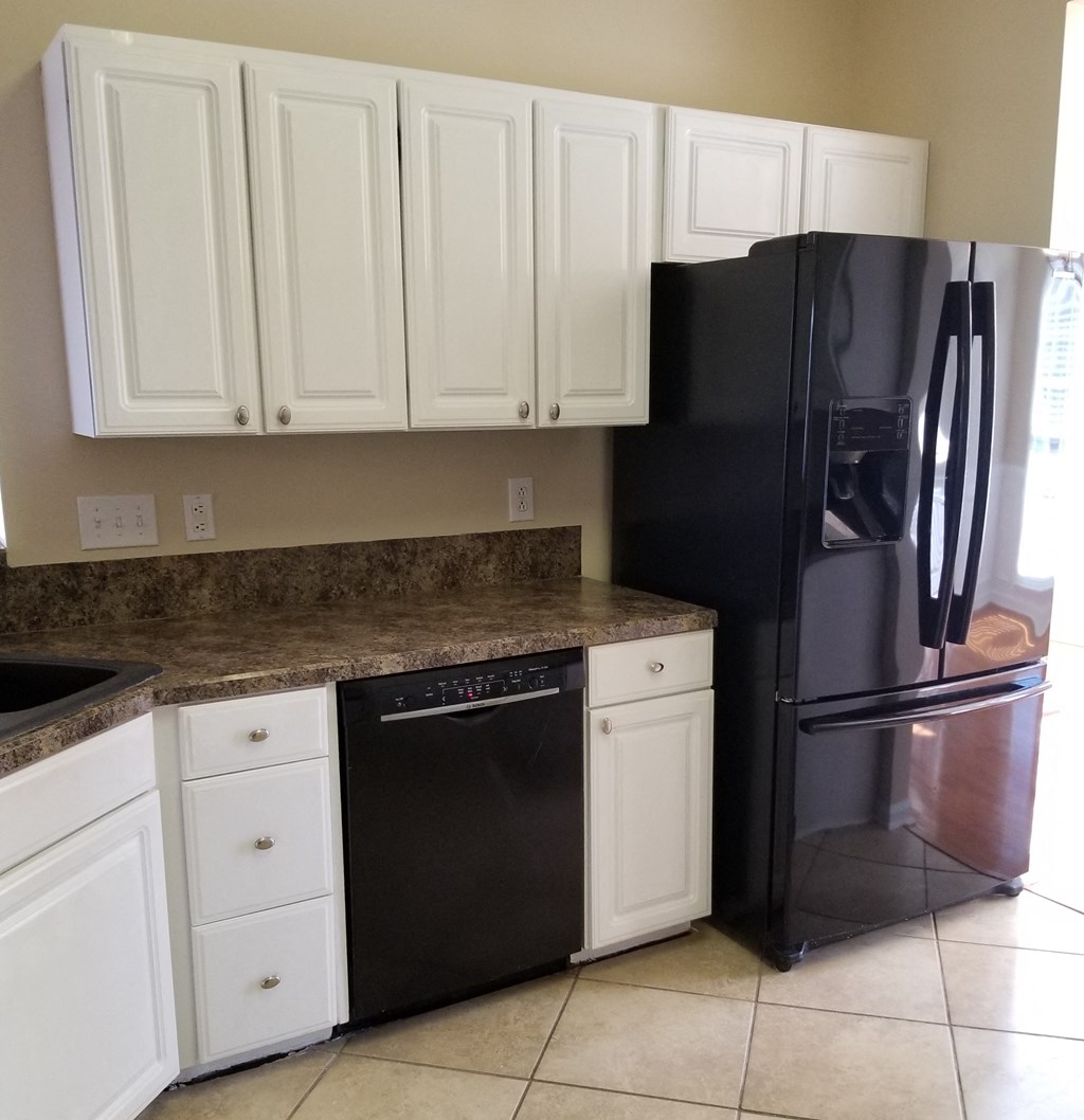 a kitchen with white cabinets and a black refrigerator