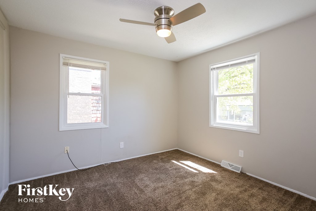 an empty room with a ceiling fan and two windows