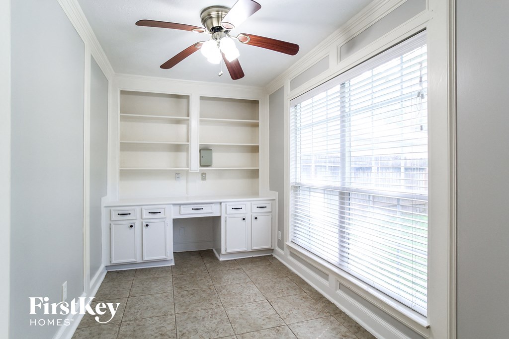 a home office with white cabinets and a ceiling fan