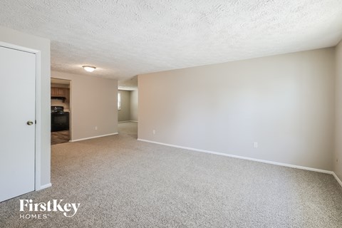 a spacious living room with white carpet and a door to the kitchen