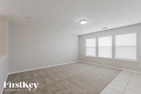 A spacious room with a carpeted floor and a window with blinds.