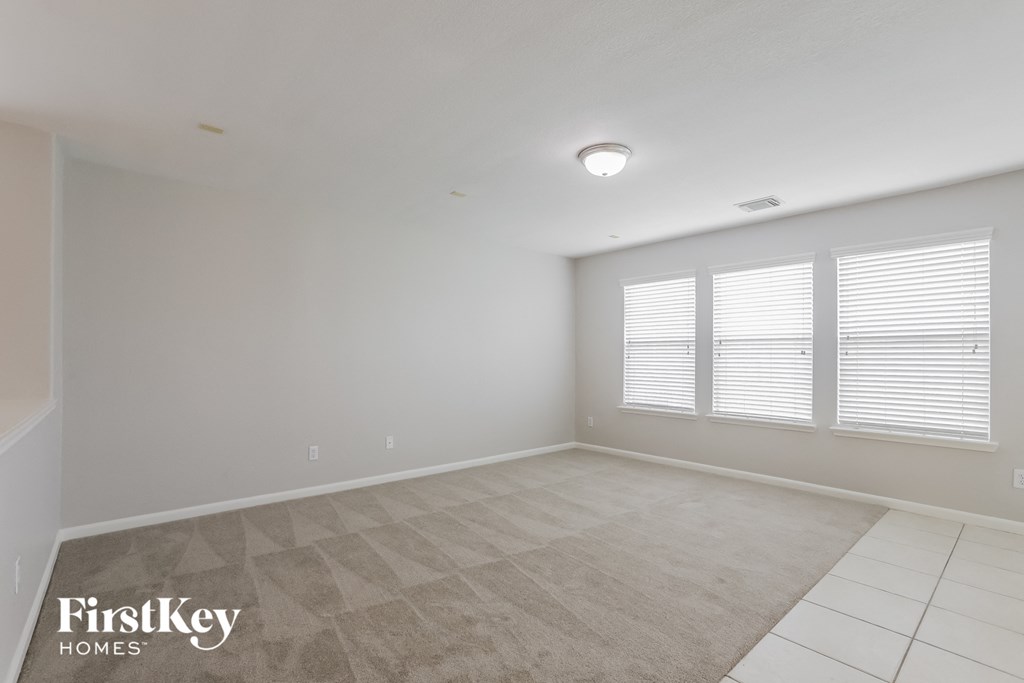 A spacious room with a carpeted floor and a window with blinds.