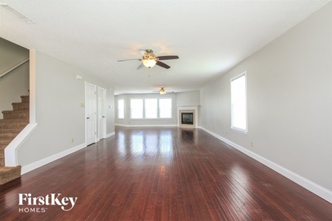 A spacious room with wooden floors and a staircase on the left side.