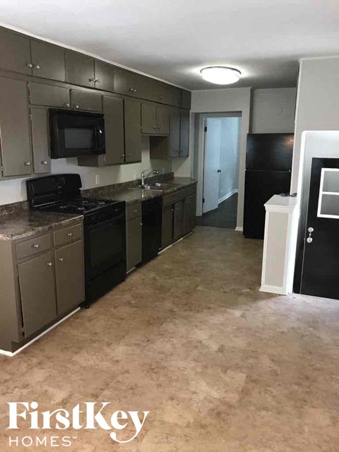 A kitchen with a black fridge and a black stove top.
