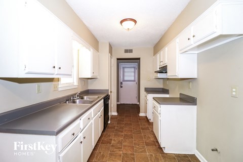 a kitchen with white cabinets and counters and a door to a hallway