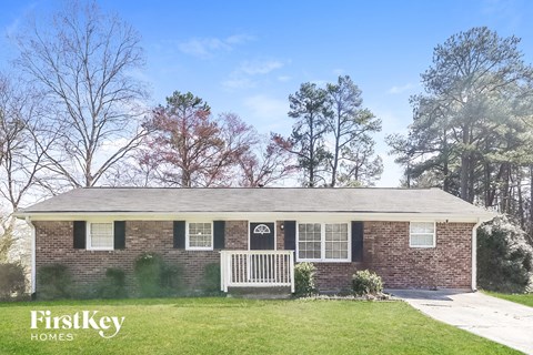 A brick house with a porch and a tree with red leaves in front of it.