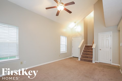 an empty living room with a ceiling fan and a staircase
