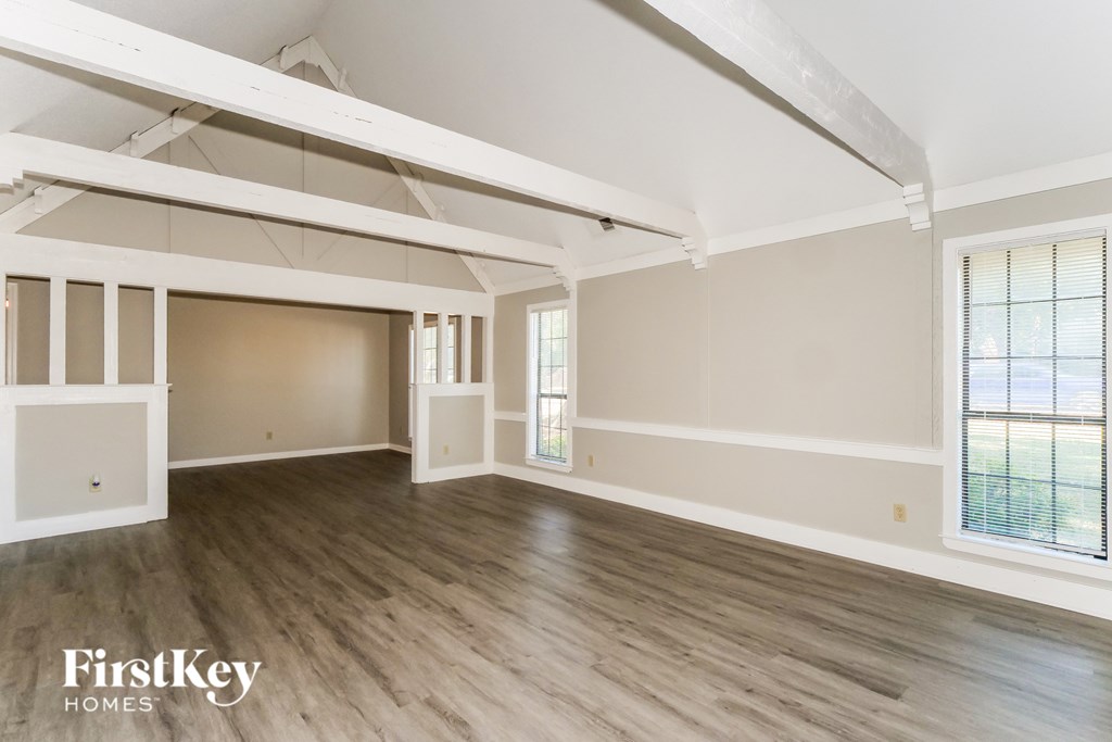 A spacious room with wooden flooring and white walls, with a large window on the right side.