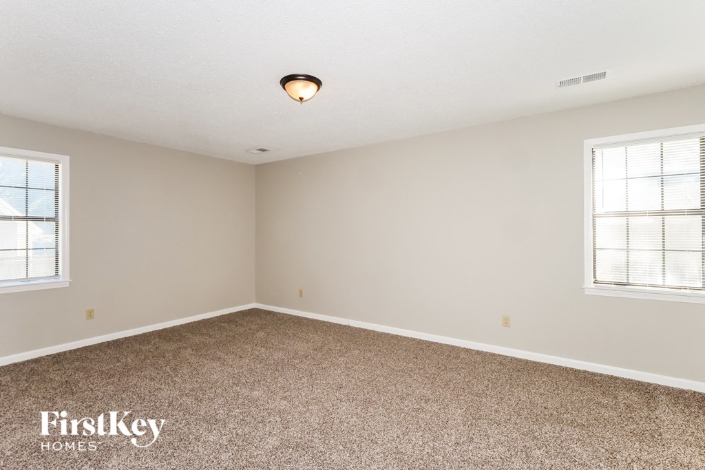 A room with a carpeted floor and two windows.