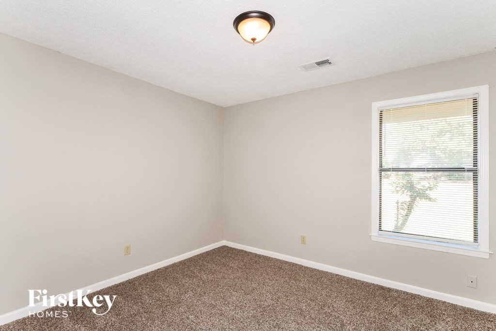 A room with a carpeted floor, a window with blinds, and a ceiling light.