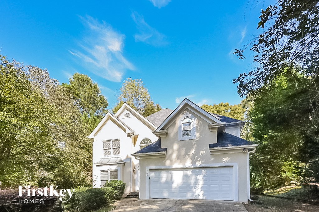 A white house with a black roof and a garage door is surrounded by trees.