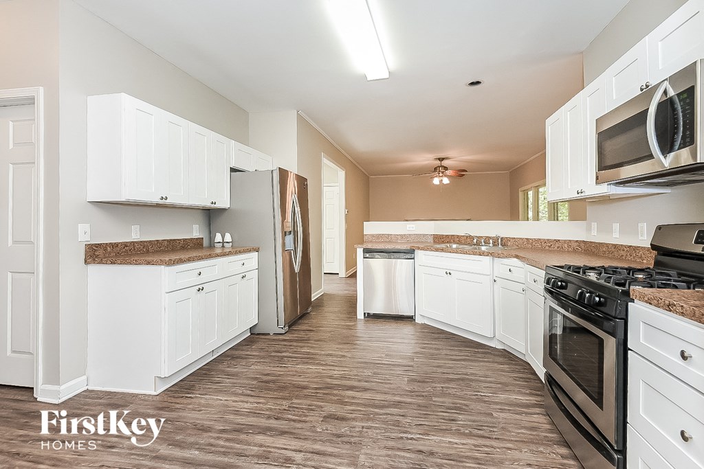 A kitchen with white cabinets and appliances, and a wooden floor.