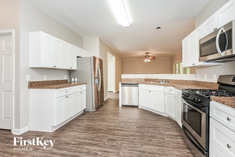 A kitchen with white cabinets and appliances, and a wooden floor.