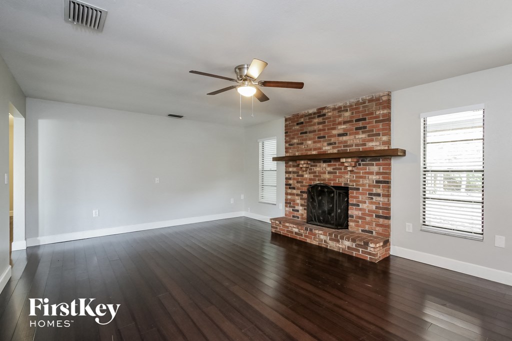 an empty living room with a brick fireplace and a ceiling fan