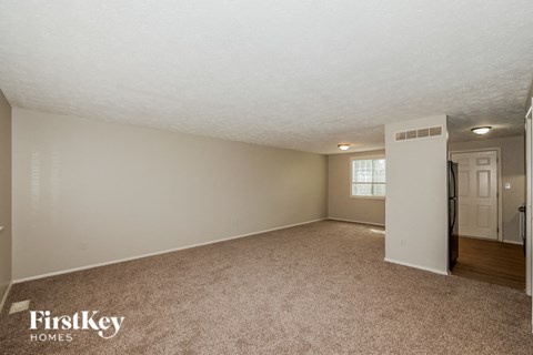 A spacious empty room with a carpeted floor and a door on the right side.