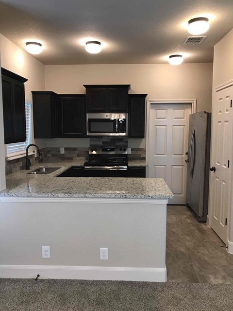 A kitchen with black cabinets and a granite countertop.