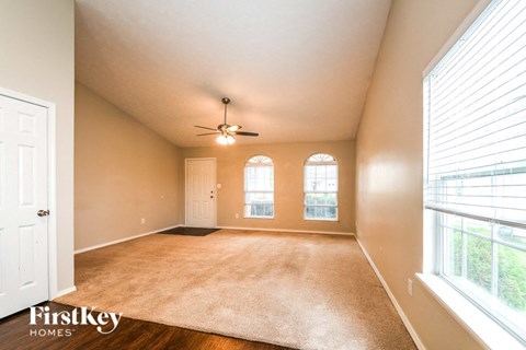 A spacious room with a carpeted floor, a ceiling fan, and a large window with blinds.