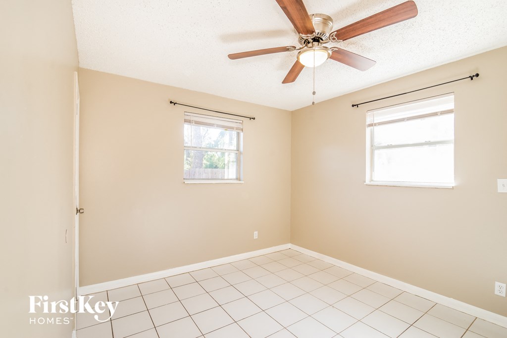 an empty room with a ceiling fan and two windows