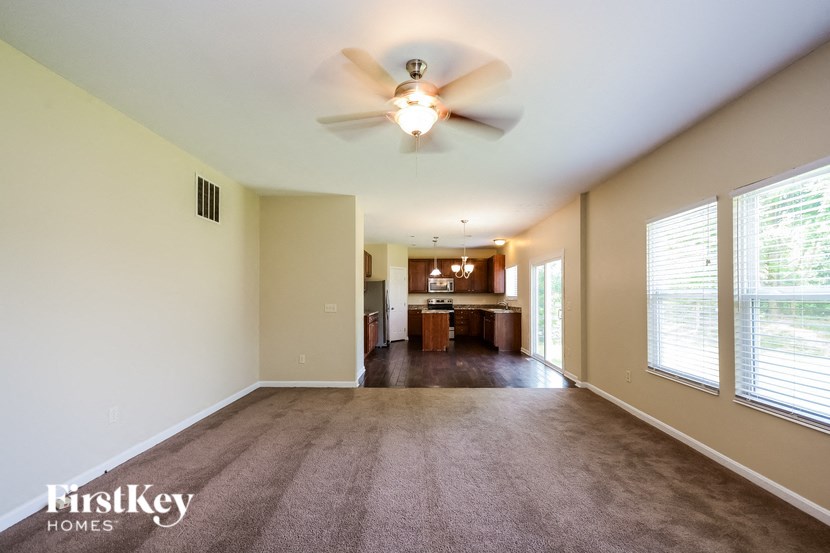an empty living room with a ceiling fan and a kitchen