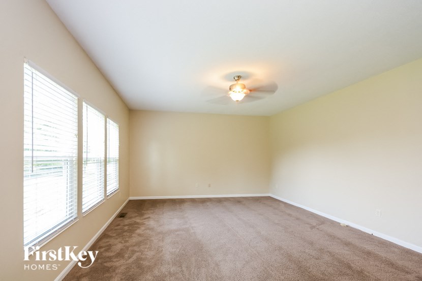 an empty living room with a ceiling fan and large windows