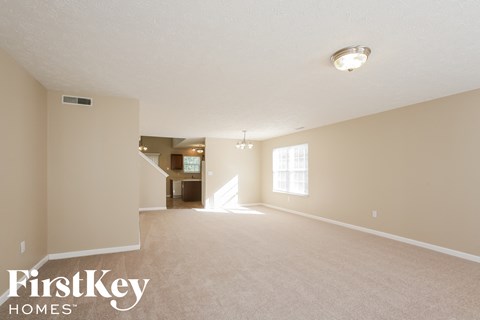 A spacious empty room with a carpeted floor and a window letting in natural light.