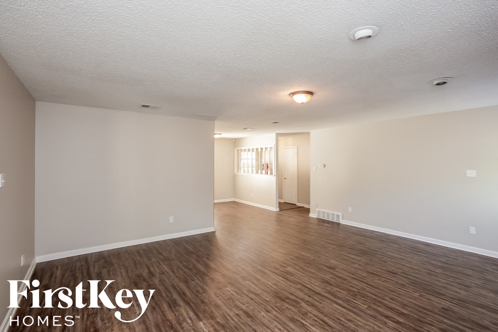 A spacious room with wooden flooring and white walls, with a doorway leading to another room.