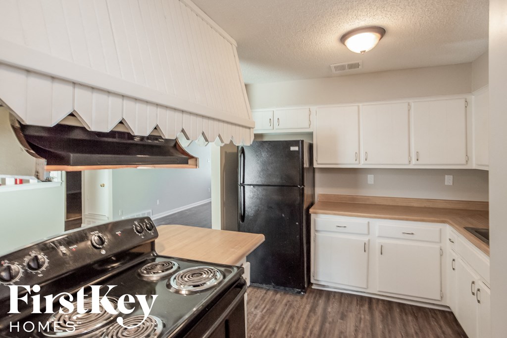 A kitchen with a stove top oven and a black refrigerator.