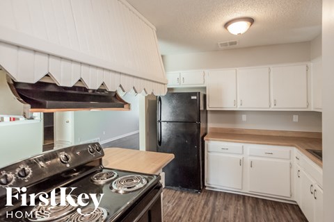 A kitchen with a stove top oven and a black refrigerator.