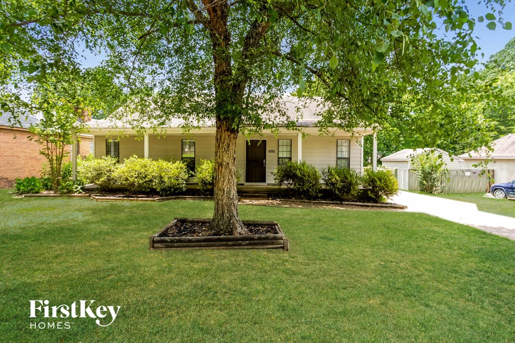A tree in a flower bed in front of a house.