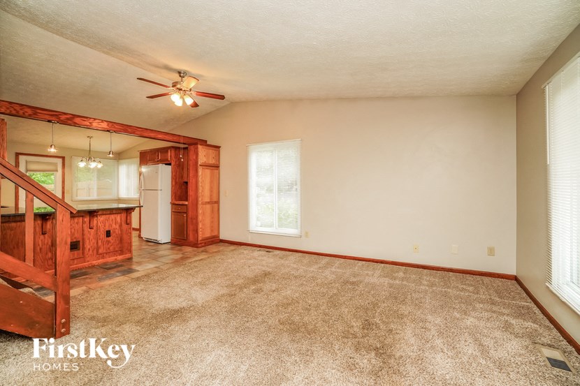 an empty living room with a kitchen and a ceiling fan