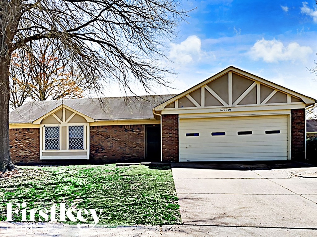 A house with a garage and a tree in front of it.
