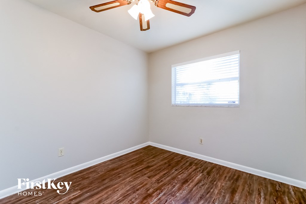 a bedroom with white walls and wood floors and a window