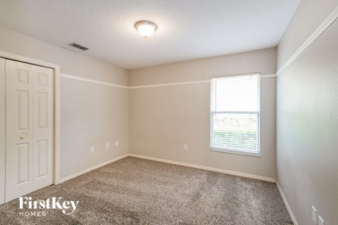 the bedroom of a house with carpet and a window