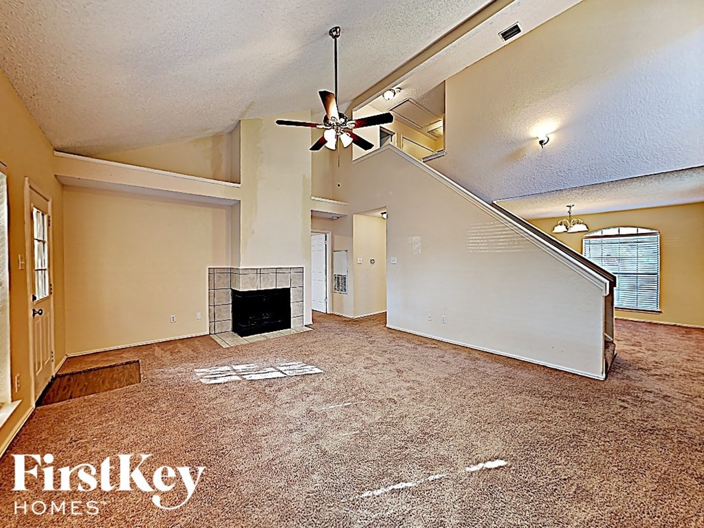 an empty living room with a fireplace and a ceiling fan