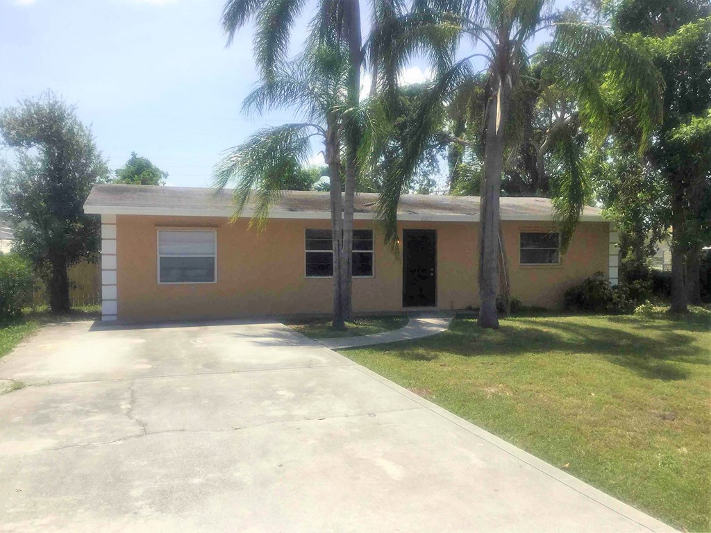 A small building with a yellow and beige exterior is surrounded by palm trees.
