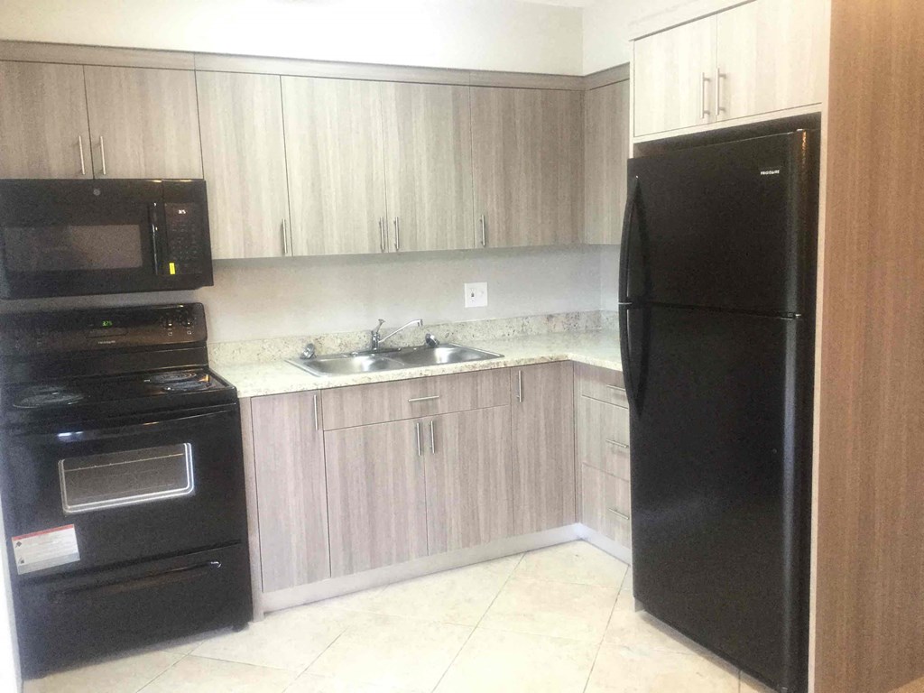 A black refrigerator stands in a kitchen with wooden cabinets and a black oven.