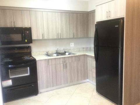 A black refrigerator stands in a kitchen with wooden cabinets and a black oven.
