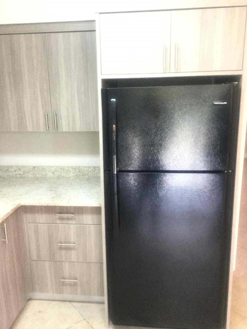 A black fridge in a kitchen with wooden cabinets.